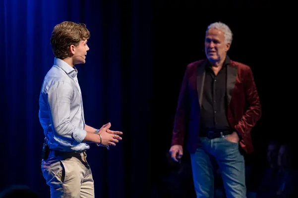 Twee sprekers in gesprek op een blauw verlicht podium