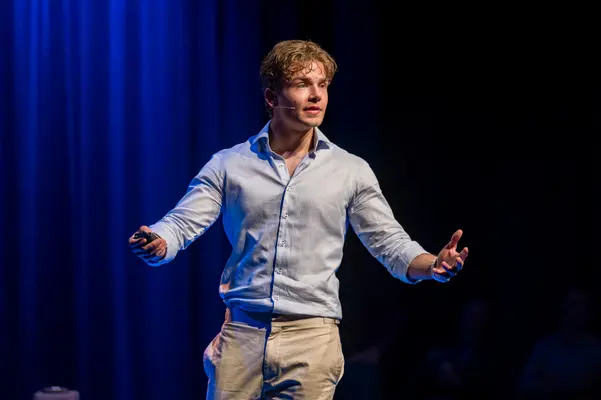 Spreker met gespreide armen op een blauw verlicht podium