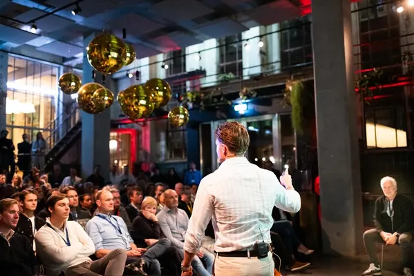 Spreker voor een volle zaal onder gouden discoballen