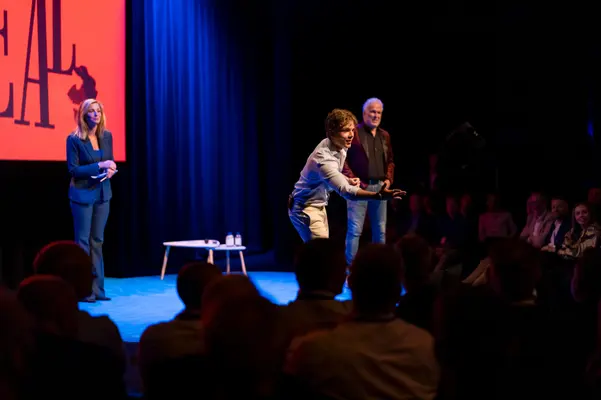 Spreker leunt naar het publiek tijdens een interactief moment op het podium
