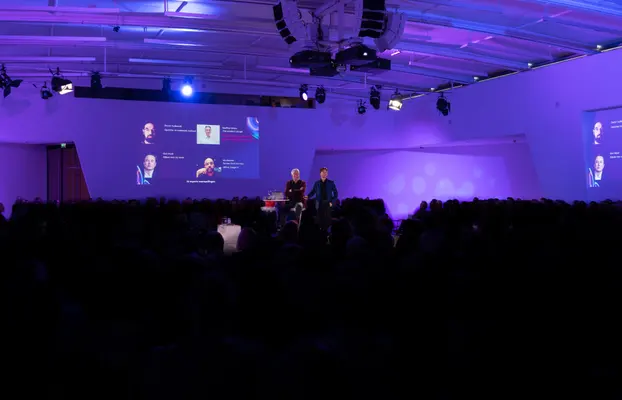 Volle zaal in paars licht tijdens een AI-lezing met twee sprekers op het podium
