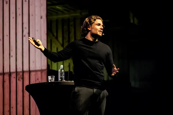 Spreker op een podium met houten decor tijdens een AI-lezing