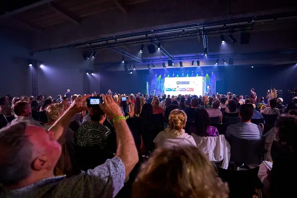 Volle zaal met publiek dat foto’s maakt van het podium tijdens een AI-lezing