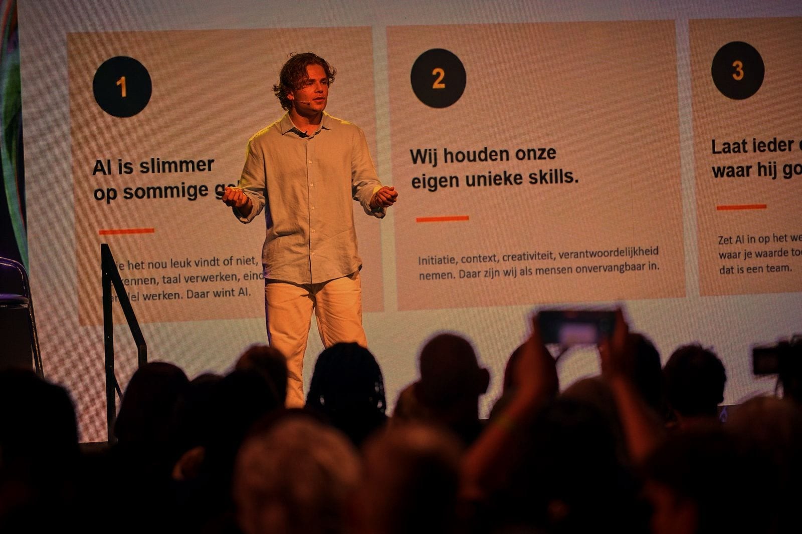 Speaker on stage in front of a large LED screen showing three key points about AI and human skills