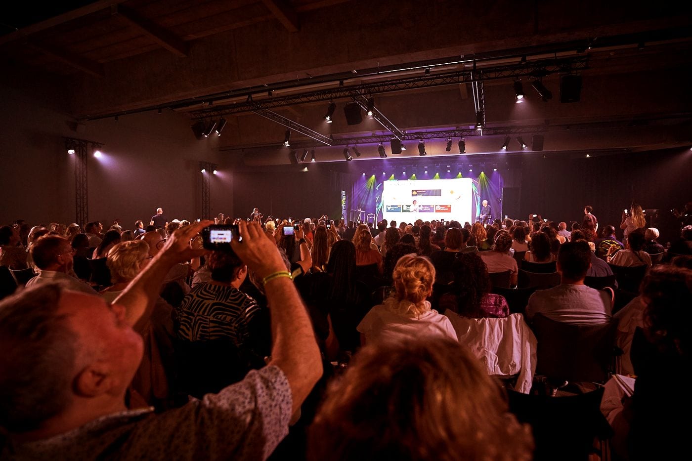 A packed room with the audience photographing the stage during an AI keynote