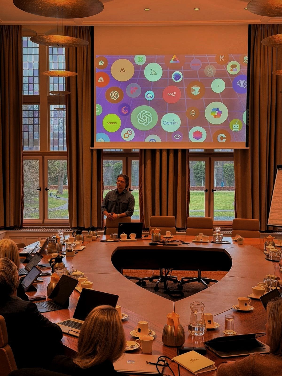 AI session with a leadership team around a large boardroom table, AI tools on screen
